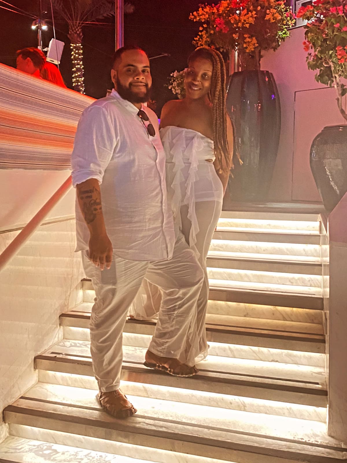A couple dressed in white pausing together on the lit marble steps of an open-air venue at night
