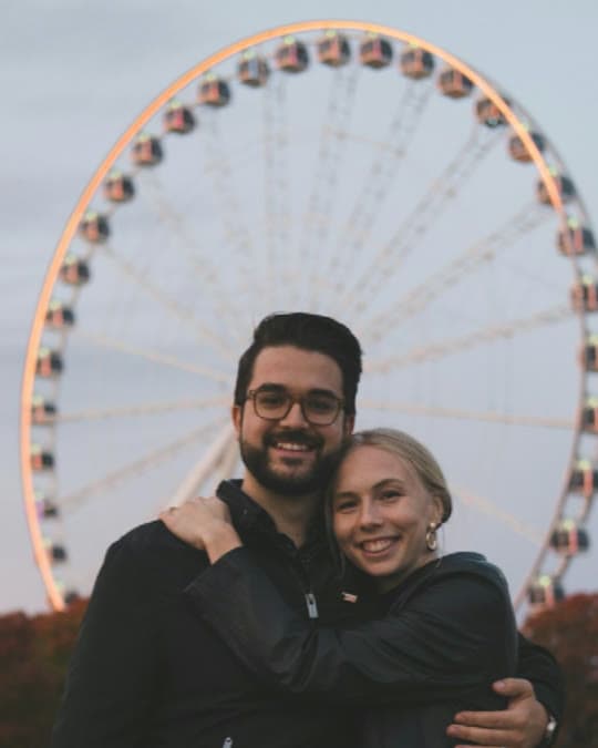 A couple embracing in front of a lit Ferris wheel at dusk on a getaway