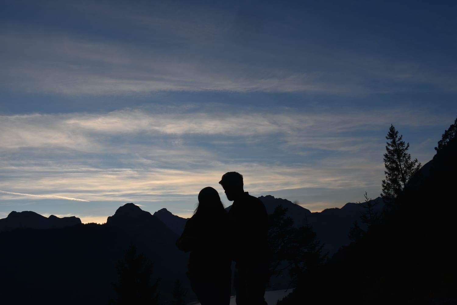 A couple in silhouette at twilight overlooking mountains and a lake on a getaway