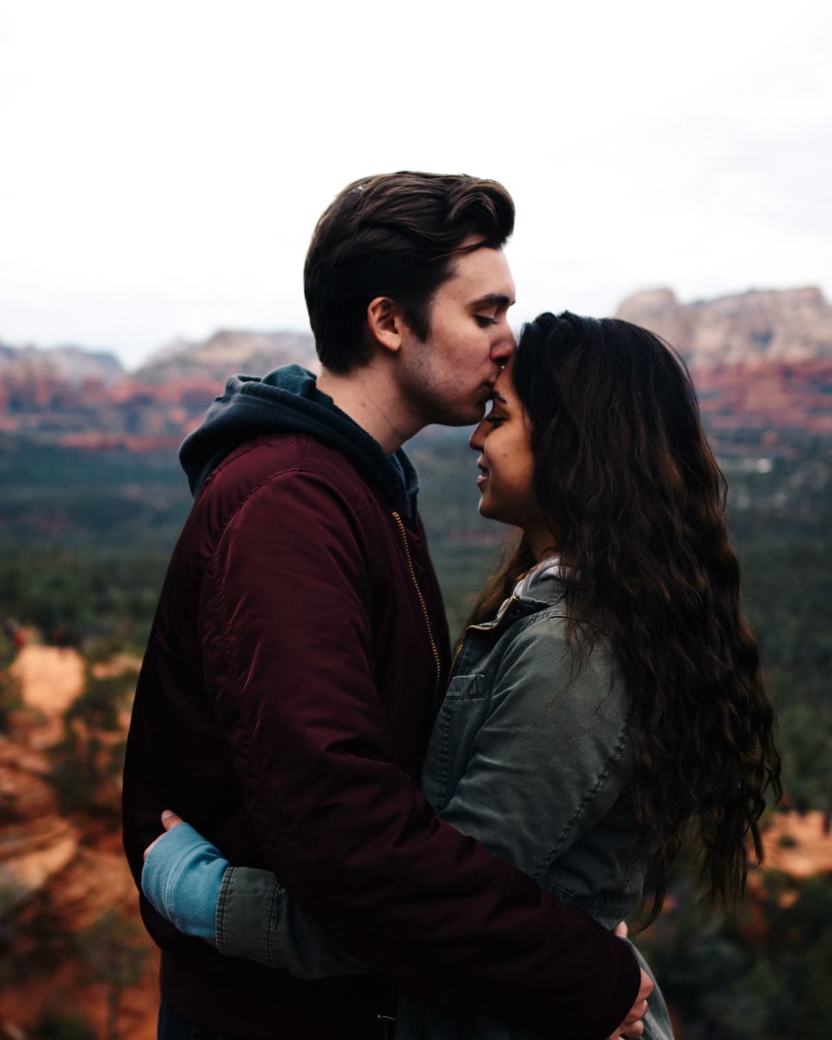 A couple embracing on a mountaintop overlook, sharing a forehead kiss