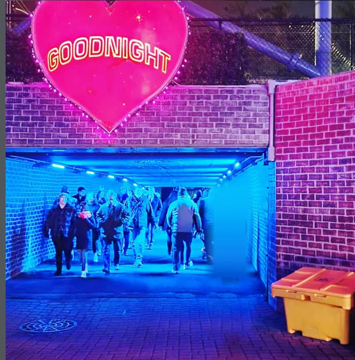A pink neon heart reading GOODNIGHT above a blue-lit brick tunnel as a crowd walks out of Kennywood at night