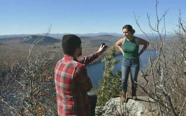 A mountaintop proposal overlooking a lake, one partner kneeling with the ring box out