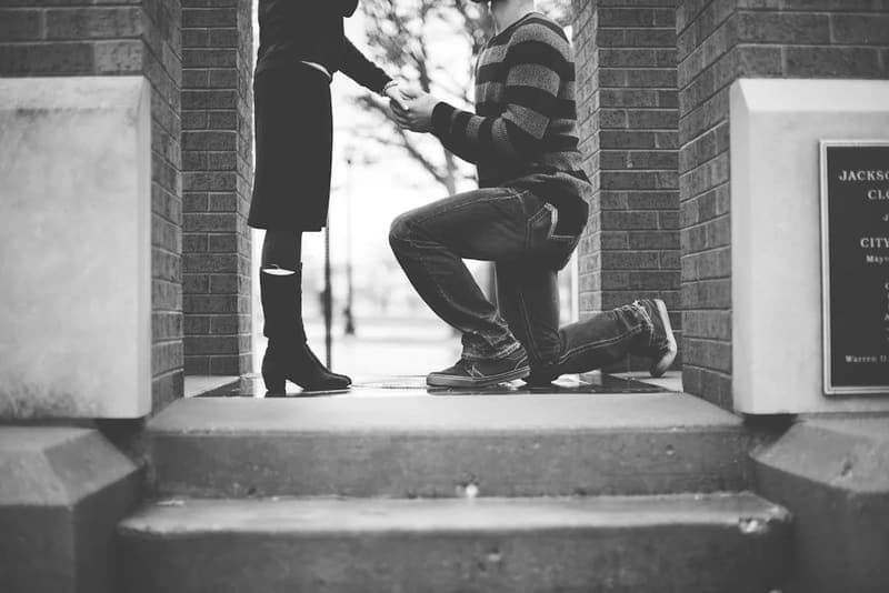 A man on one knee proposing to his partner on brick steps
