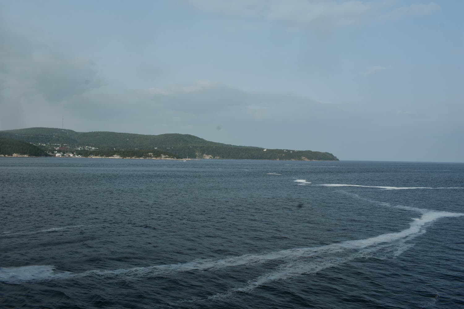 A village on a wooded headland seen across open water from the deck of a boat