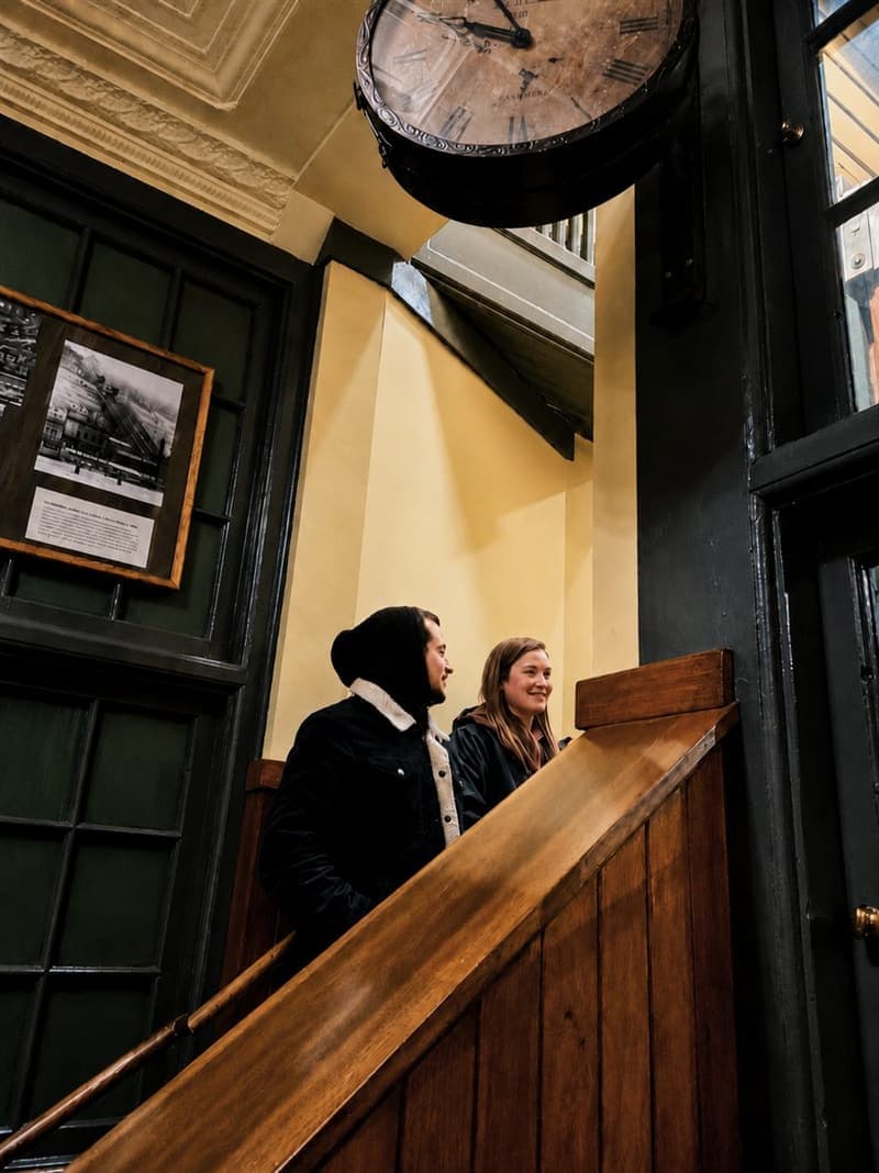 A couple dressed in vintage clothes beside a wooden staircase and station clock
