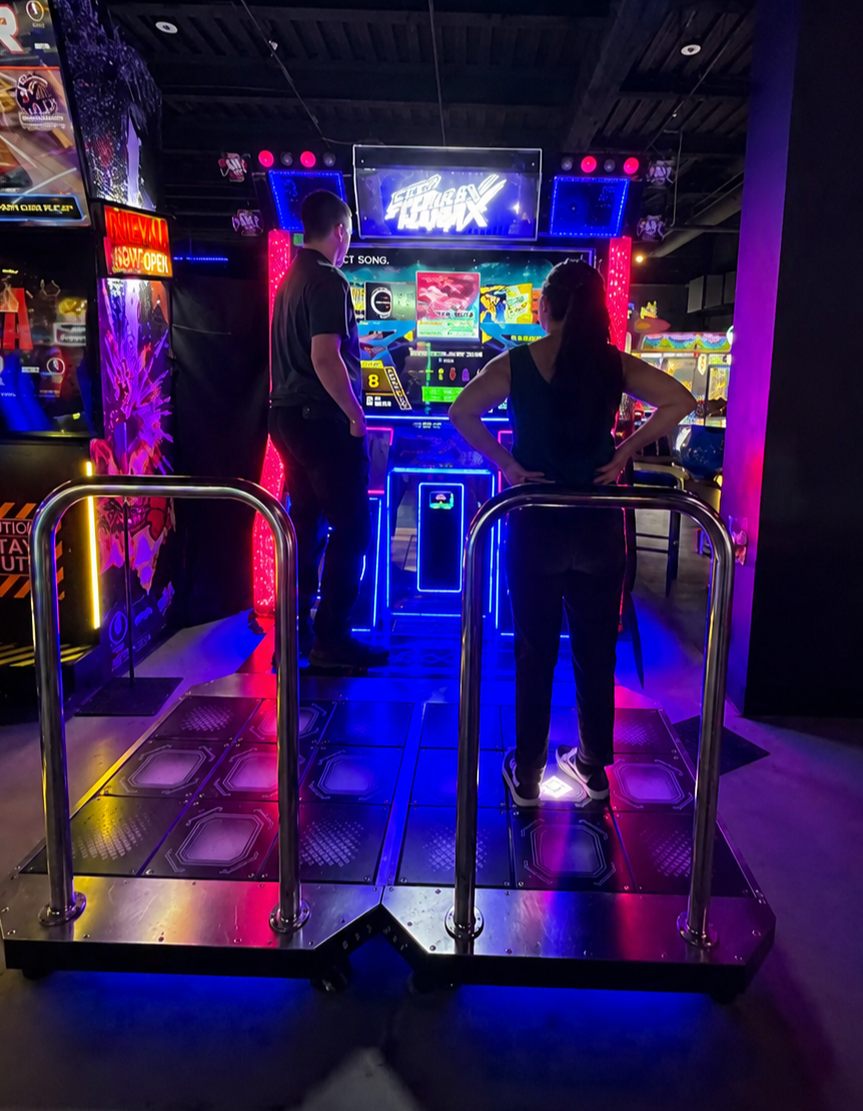A couple playing a neon-lit dance arcade game together