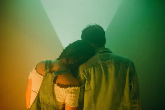 A couple leaning on each other, seen from behind in soft colored light